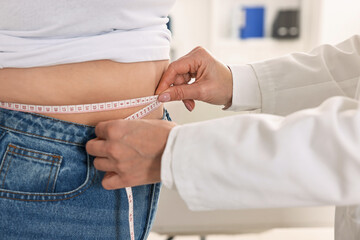 Weight loss. Nutritionist measuring patient's waist with tape in clinic, closeup