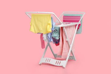 Drying rack with fresh clean laundry on light pink background