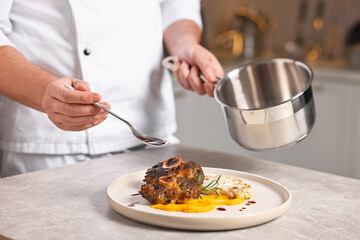 Professional chef adding sauce to delicious dish at table indoors, closeup