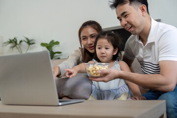 Family sharing popcorn and enjoying a movie together on a laptop.