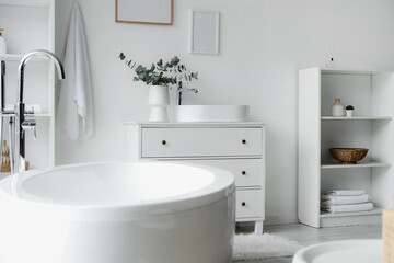 Bathtub and chest of drawers with sink in interior of light bathroom