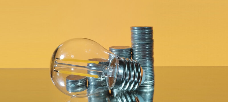 Investing in energy efficiency lightbulb and coins against yellow background business concept studio environment close-up view