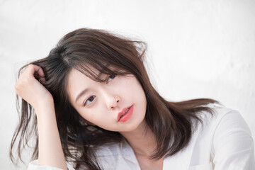 Naklejka premium 白シャツで髪をかき上げる爽やかな女性 ヘアケアや美容やビューティークローズアップ アンニュイな表情