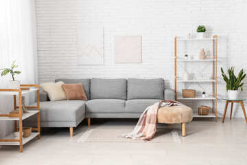 Interior of light living room with grey sofa and shelving units near white brick wall