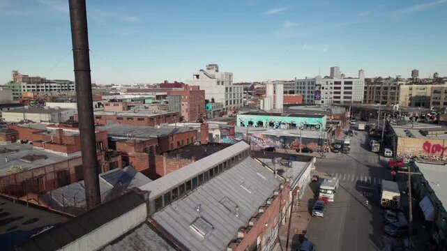 Gritty graffiti covered industrial buildings in Bushwick, Brooklyn, NY. Drone shot with factory smokestack in foreground, 4K