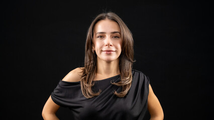 A chest-up headshot of a young, brown-haired woman taken in a studio setting with a black background