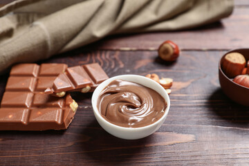 Bowl of sweet chocolate spread and hazelnuts on wooden background