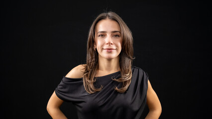 A chest-up headshot of a young, brown-haired woman taken in a studio setting with a black background