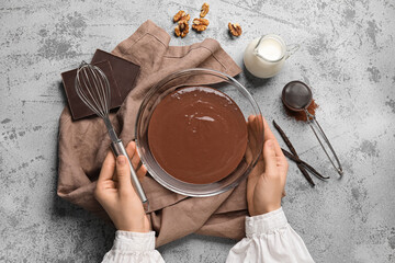 Female hands with whisk and bowl of hot chocolate on grunge grey background. Top view