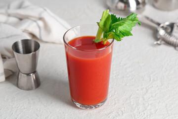 Glass of bloody mary with celery and measuring cup on white background