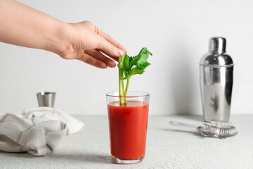 Woman putting celery into glass of bloody mary on white background