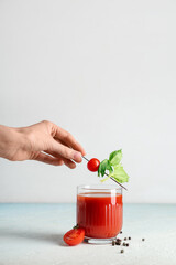 Female hand with glass of bloody mary, celery, tomatoes and peppercorns on light background