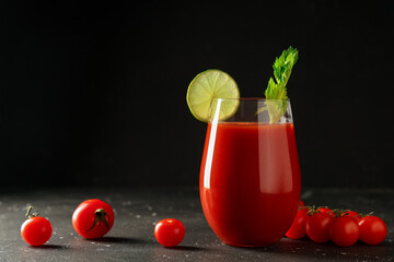 Glass of bloody mary with celery, lime slice and tomatoes on dark background