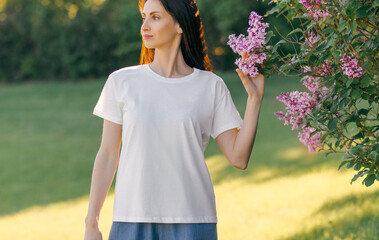 A young woman wearing a white plain T-shirt outdoors, green nature background. Mockup for design, template. Front view