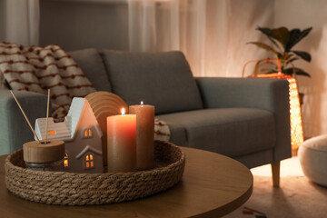 Tray with burning candles and reed diffuser on table in living room at night, closeup