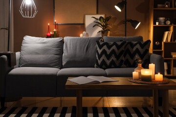 Interior of dark living room with sofa, glowing lamps and burning candles