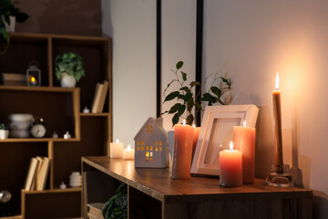 Burning candles with frame on shelf in room at night
