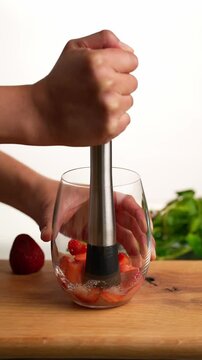 Vertical video, Strawberry mojito cocktail, muddling strawberries, sugar and lime juice to prepare a mojito, slow motion
