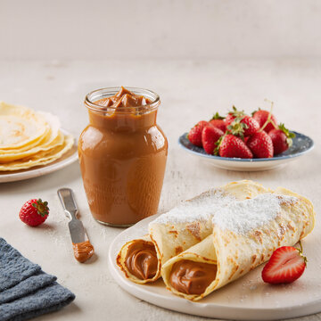 panqueques rellenos de dulce de leche con frasco de dulce de leche y frutillas