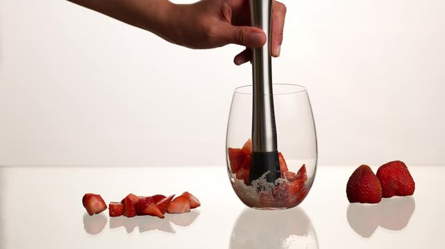 Strawberry mojito cocktail, muddling strawberries, sugar and lime juice to prepare a mojito