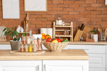 Jars with different spices, plant and vegetables on table in kitchen