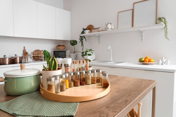 Jars with different spices, cooking pot and plant on table in kitchen