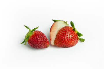 strawberries are arranged in a heart shape on a white background. The berries are red with green stems, some showing a transition to lighter, unripe areas. The image is a top-down view