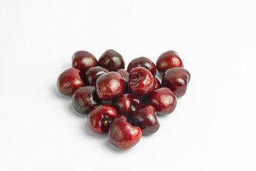 This image shows a group of dark red cherries arranged in a loose, heart-like shape on a white background