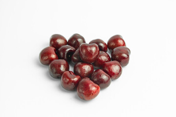 This image shows a group of dark red cherries arranged in a loose, heart-like shape on a white background