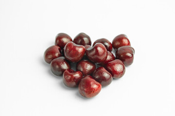 This image shows a group of dark red cherries arranged in a loose, heart-like shape on a white background