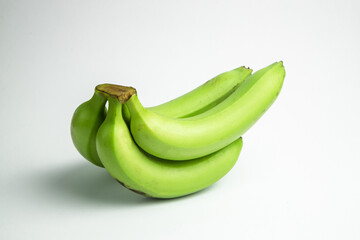 A bunch of green bananas are stacked against a white background, showing a close-up view of the unripe fruit © VanK Ngn