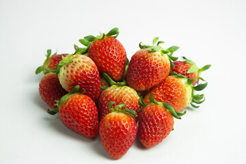 strawberries are arranged in a heart shape on a white background. The berries are red with green stems, some showing a transition to lighter, unripe areas. The image is a top-down view