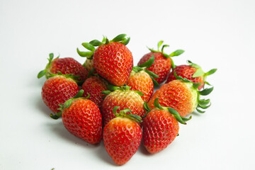 strawberries are arranged in a heart shape on a white background. The berries are red with green stems, some showing a transition to lighter, unripe areas. The image is a top-down view