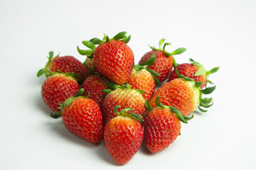 strawberries are arranged in a heart shape on a white background. The berries are red with green stems, some showing a transition to lighter, unripe areas. The image is a top-down view
