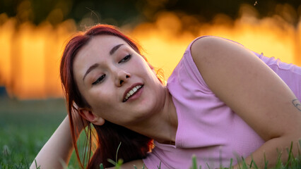 A beautiful red-haired young woman models stylishly in the park on a summer day, posing stylishly...