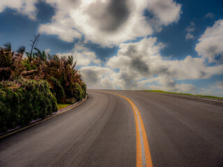Street with a steep climb reveals a large open blue sky with large puffy clouds giving the appearance of driving into heaven