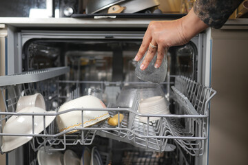 Hand placing glass in dishwasher during kitchen cleanup