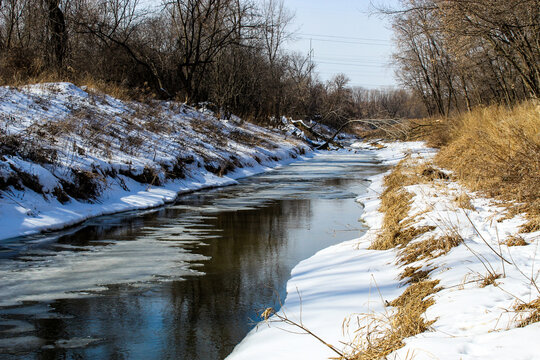 an icy creek melting in early spring with snow banks water landscape late winter.  snowbanks by a creek watershed beauty in nature ecology aquatic midwestern United States backdrop.