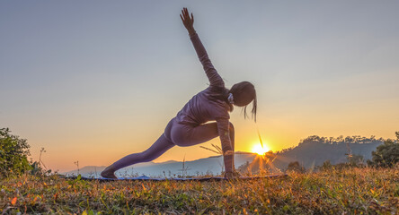 Young beauty girl doing yoga pose on mountain sunset background.