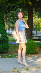 A beautiful red-haired young woman modeling stylishly in a wooded area on a summer day, giving chic...