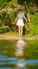 A beautiful red-haired young woman models stylishly by a river in a wooded area on a summer day,...
