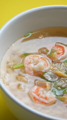 rice soup with shrimp in white bowl on yellow background