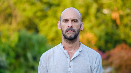 A middle-aged handsome businessman looking angrily at the camera in a tree-lined park on a summer...