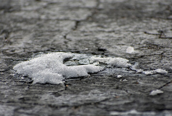 A clump of snow on cracked blacktop.