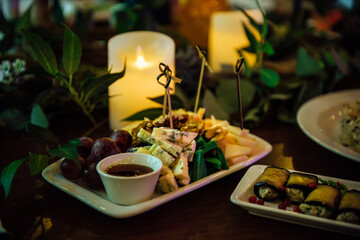 Assorted cheeses on a white plate with honey, walnuts and red grapes. A plate with a variety of cheeses on the table in the restaurant, decorated with green stems and leaves