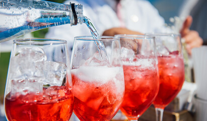The bartender pours soda into a glass of wine with ice in close-up. Creating a red cocktail, wine,...