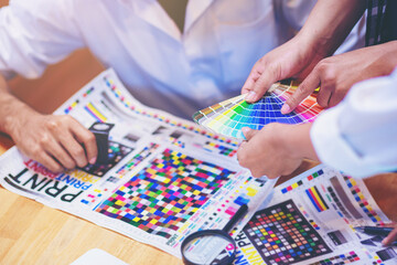 Team graphic designer checking print quality of media graphics proof print and color guides in...