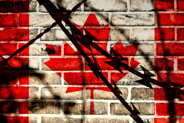 A wall and flag of Canada behind the barbed wire