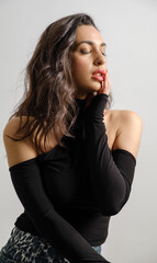 Fototapeta premium In a studio setting with a white background, a young black-haired woman wearing a black blouse and jeans strikes an artistic pose