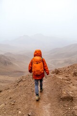 Fototapeta premium Mindful Wilderness Escape Solo Hiker in Vibrant Orange Attire on Misty Atlas Mountain Path - Adventure Travel Content and Outdoor Wellness Marketing